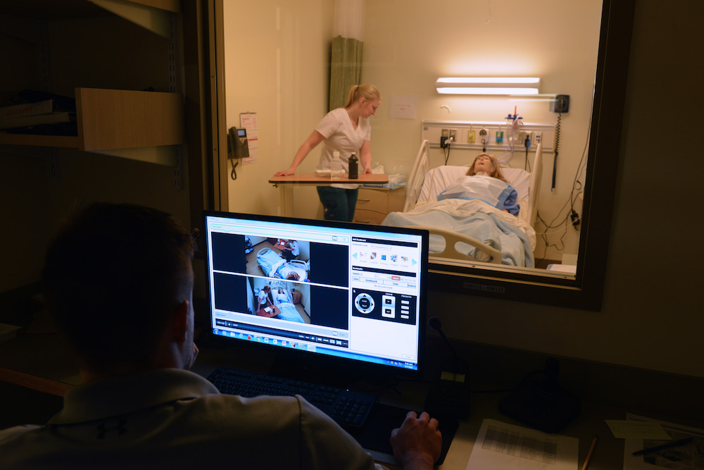 A computer monitors a female nursing student working with an adult patient simulation